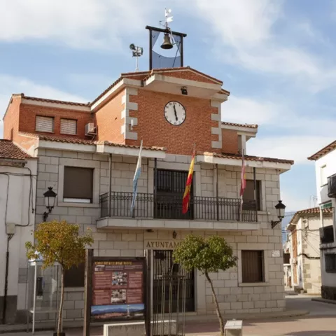 Edificio municipal con reloj y balcones en una calle tranquila.