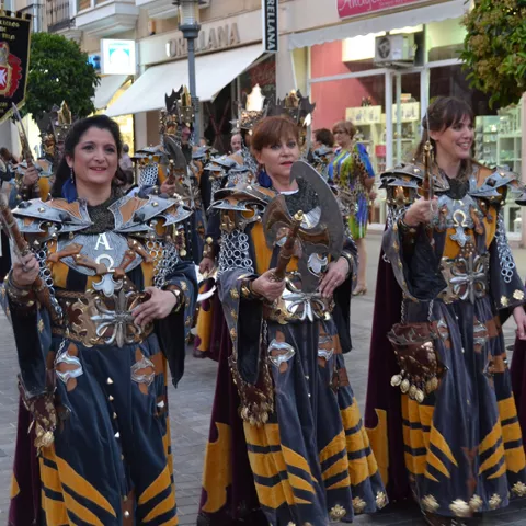 Grupo de mujeres desfilando con armaduras ornamentales y hachas decorativas