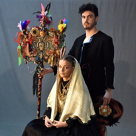 Pareja con trajes tradicionales y vara decorada con cintas y plumas.