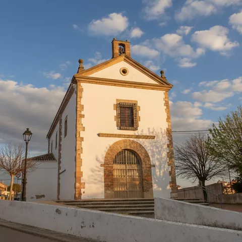 Capilla blanca con portada de ladrillo y cielo abierto.