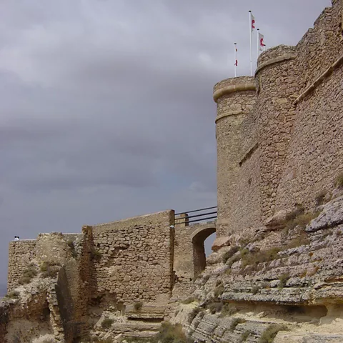 Muralla sobre roca, con paso elevado y torre defensiva.
