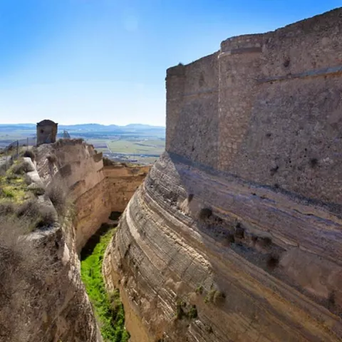 Muralla de piedra junto a un profundo foso excavado en la roca