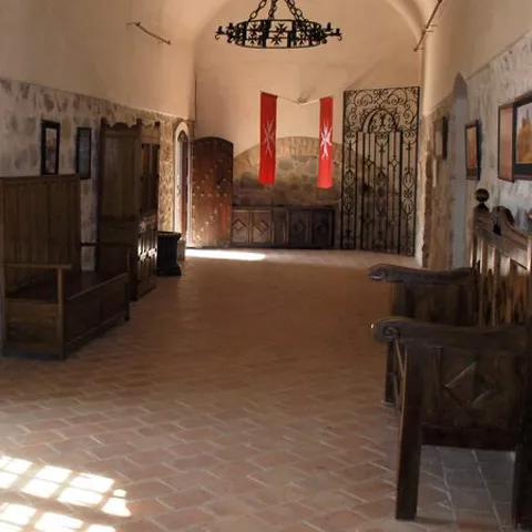 Sala interior con muros de piedra, bancos de madera y luz natural.