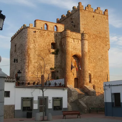 Fortaleza iluminada al atardecer, con banderas en la entrada y plaza en primer plano.