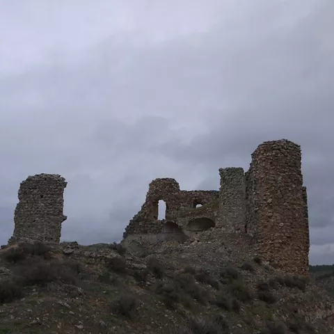 Ruinas de castillo en cresta rocosa bajo cielo nublado.