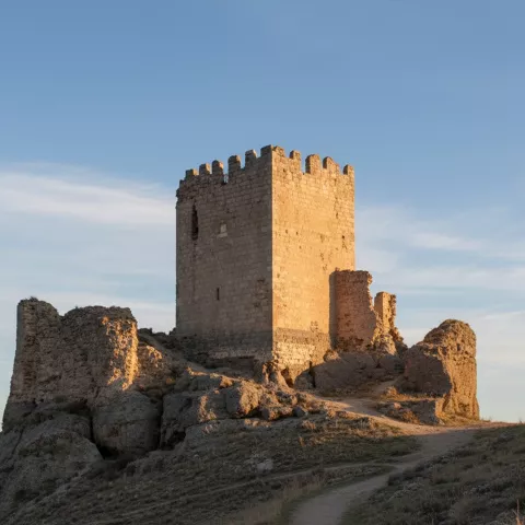 Torre cuadrada de piedra junto a muros derruidos.