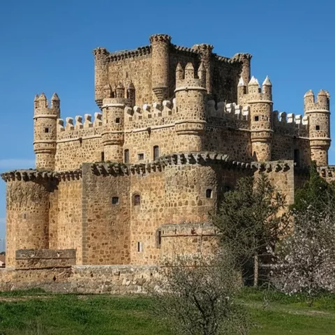 Castillo de piedra con torres circulares y almenas sobre césped verde.