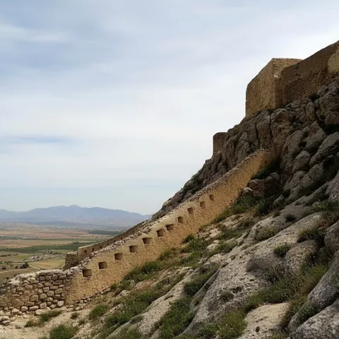 Tramo de muralla sobre rocas, con vista panorámica de valle y montañas lejanas.