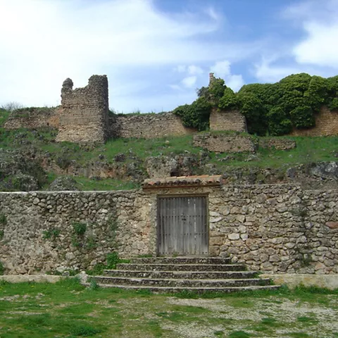 Muralla de piedra con restos de torres sobre una colina y acceso con escaleras.