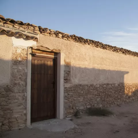 Muro largo de piedra y cal con puerta de madera, junto a un camino de tierra.