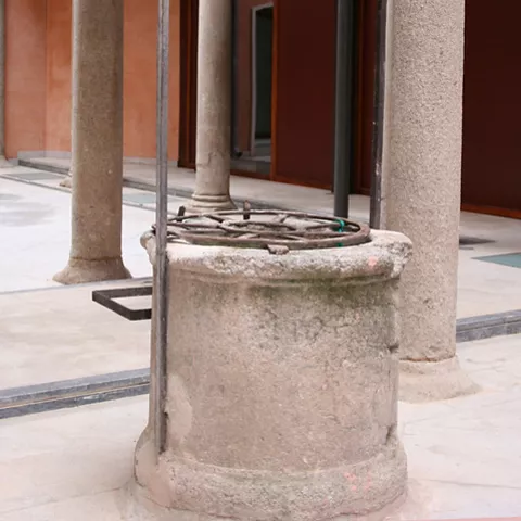 Pozo de piedra con estructura metálica en patio porticado.