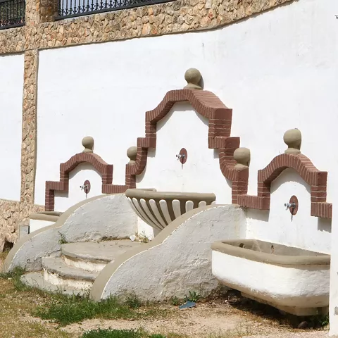 Fuente tradicional de pared con pilas de piedra y arcos decorativos.