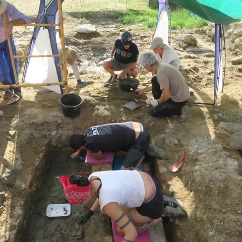Equipo de arqueología excavando cuidadosamente en una zanja de un yacimiento.