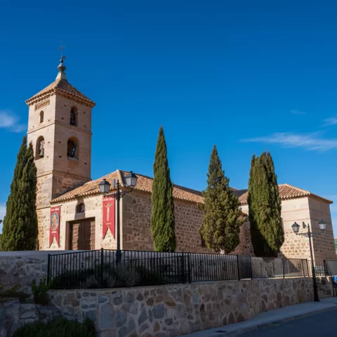 Iglesia de piedra con torre y cipreses junto a la calle