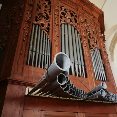 Vista lateral de órgano con tallas decorativas y tubos frontales.