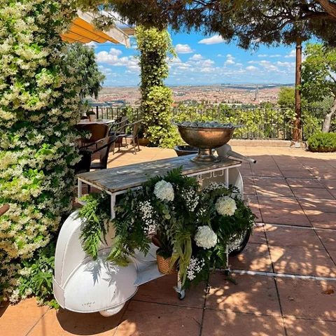 Terraza con flores blancas, carrito decorativo y vistas panorámicas de la ciudad.