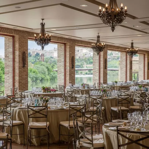 Salón para eventos con mesas redondas y grandes ventanales.