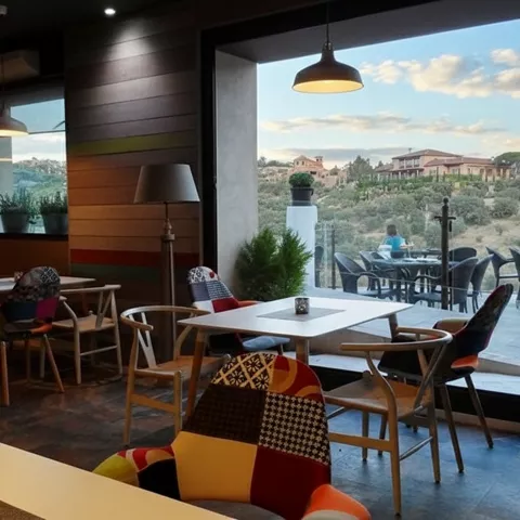 Cafetería moderna con mesas bajas y terraza con vistas.