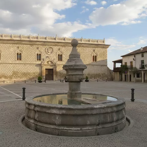 Plaza mayor con fuente central y edificio histórico de piedra