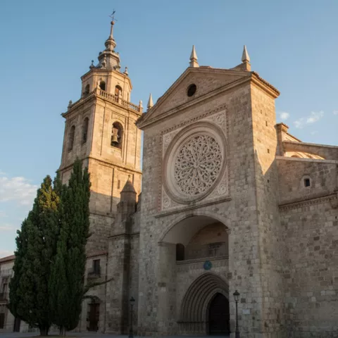 Vista lateral de iglesia histórica con torre campanario y rosetón en fachada.