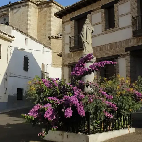 Monumento religioso rodeado de flores moradas en una plaza del pueblo.