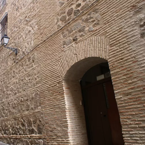 Calle estrecha con muros de piedra y ladrillo junto a un arco de entrada.