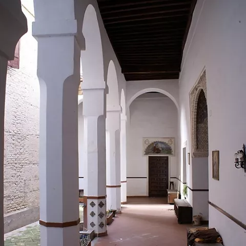 Galería con arcos blancos, techo de madera y bancos junto al patio interior.