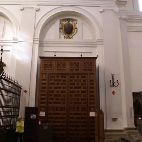 Gran puerta de madera tallada bajo arco blanco en interior religioso.