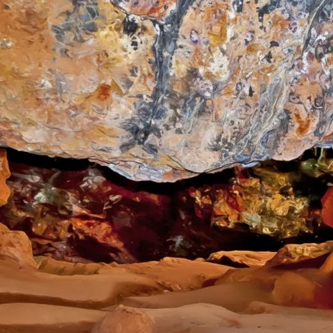 Vista interior de cueva con formaciones rocosas y suelo arenoso.