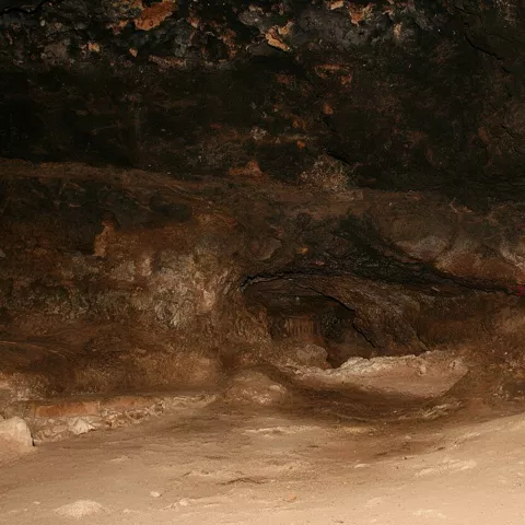 Sala interior de cueva con paredes oscuras y suelo arenoso.