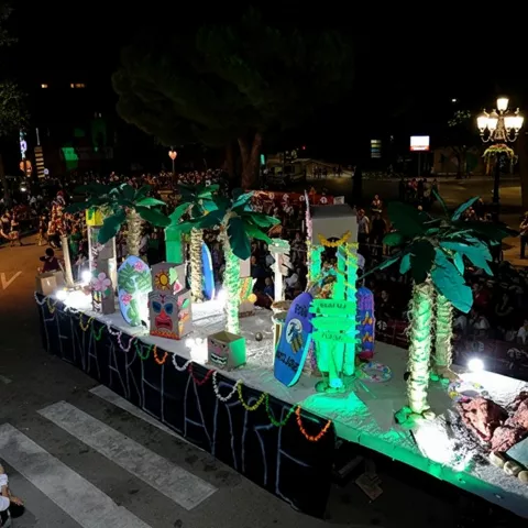 Plataforma decorada con palmeras y figuras luminosas en desfile nocturno.