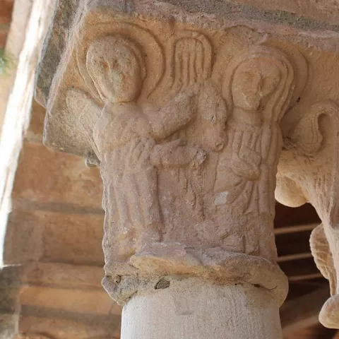 Capitel tallado con figuras en columna de piedra.