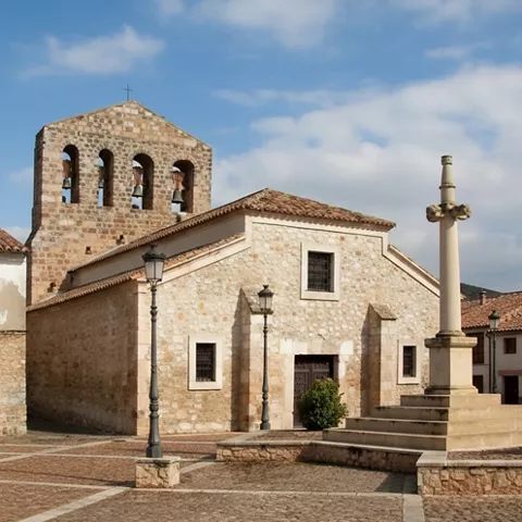 Iglesia de piedra con espadaña y cruz en plaza empedrada