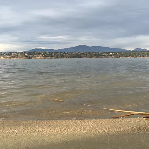 Vista del embalse desde la orilla con agua tranquila y colinas en el horizonte