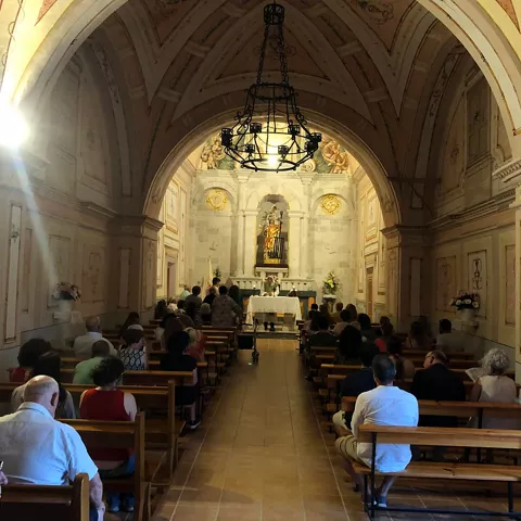 Interior de ermita con bancos de madera y personas asistiendo a una ceremonia.
