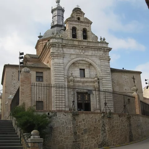 Fachada de iglesia elevada sobre escalinata con torre y cúpula al fondo.