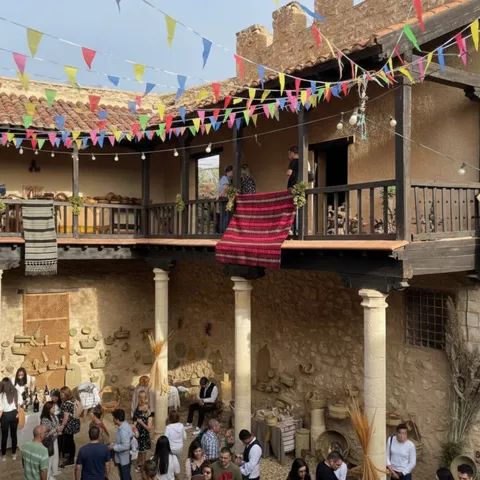Patio tradicional con banderines de colores y gente reunida junto a puestos.