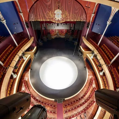 Vista cenital de teatro circular con escenario central y gradas vacías.