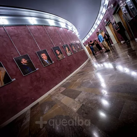 Sala interior con exposición de retratos enmarcados y personas recorriendo el espacio.