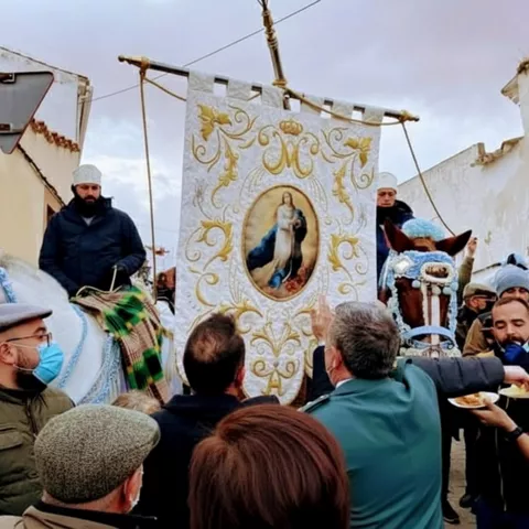 Procesión a caballo con estandarte por calle del pueblo.