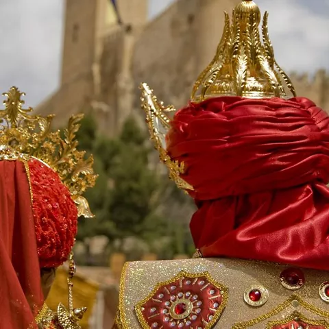 Detalle de trajes ornamentados con coronas frente a una fortaleza al fondo.