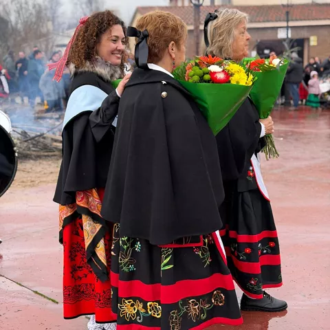 Mujeres con mantones y ramos de flores en fiesta popular.