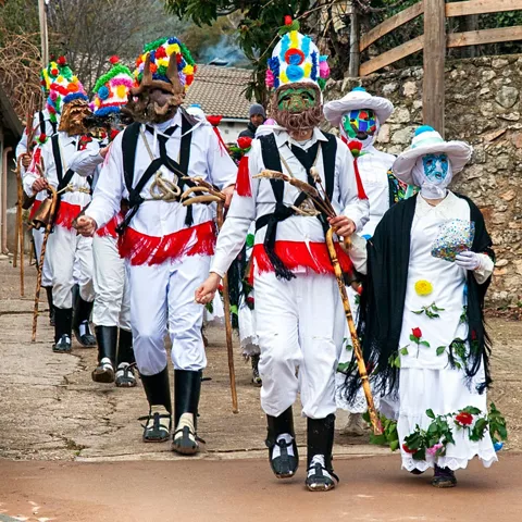 Personas con trajes tradicionales y máscaras en desfile festivo.