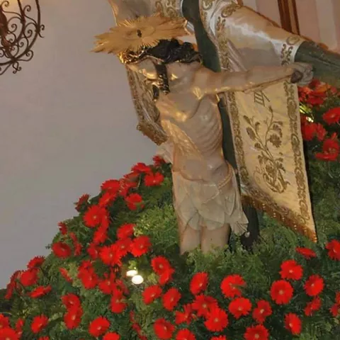 Escultura religiosa sobre una cruz decorada con flores rojas en el interior de un templo.