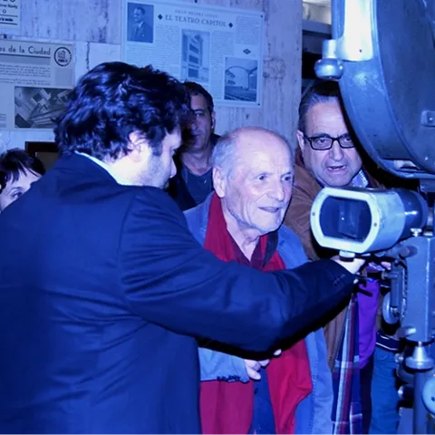Grupo de personas observando un proyector cinematográfico histórico en una sala interior.