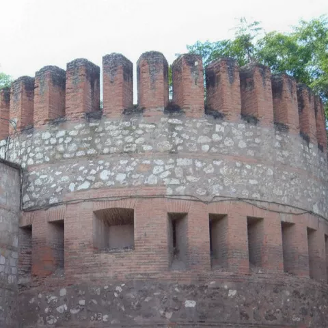 Torre circular almenada junto a muralla de piedra.