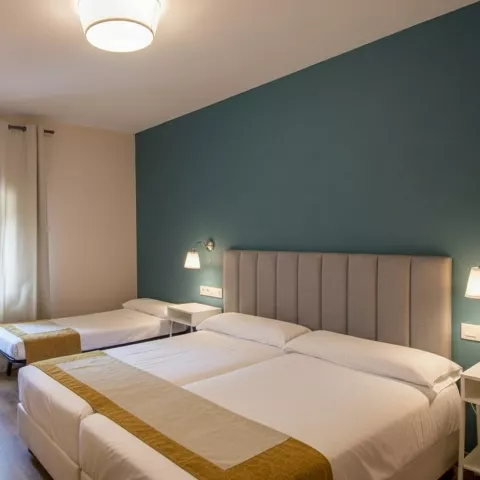 Habitación con cama doble y cama individual, escritorio y pared decorativa en tono verde.