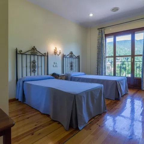 Habitación con dos camas individuales, suelo de madera y balcón con vistas a la montaña.