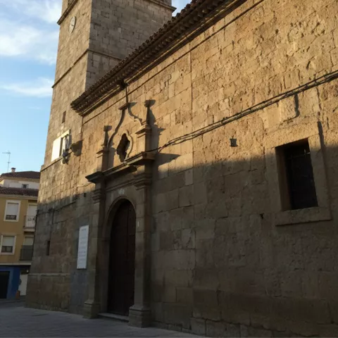 Entrada principal de iglesia de piedra con campanario y puerta de madera bajo cielo azul.