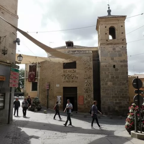 Exterior de iglesia con torre cuadrada y peatones en la plaza.